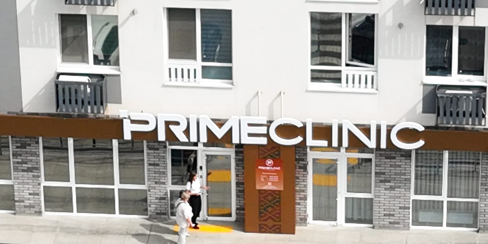 Napis PRIMECLINIC dużymi literami na parterze budynku SAVO, z własnym wejściem, pochylnią i schodami