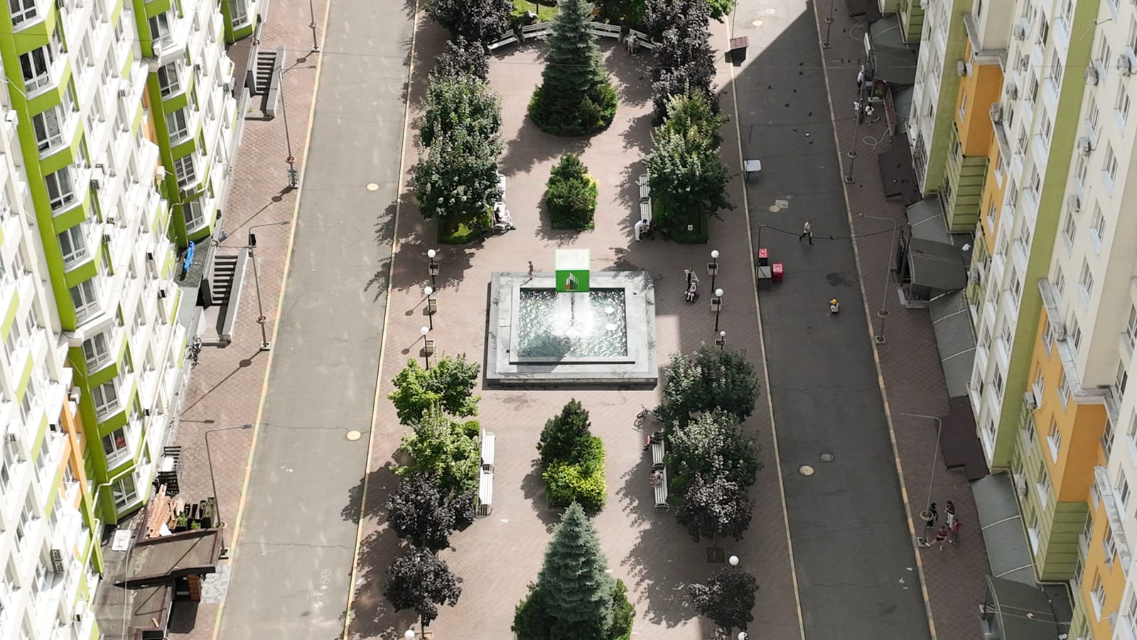 De promenade tussen twee blokken van Evromisto by SAVO van boven gezien: een werkende fontein, geschoren bomen, banken en bewoners die wandelen