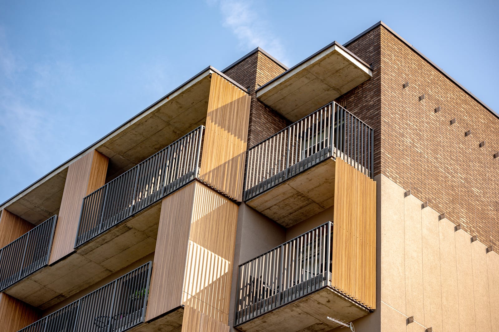 De hoek van het SAVO-gebouw in Vilnius tegen een onbewolkte hemel: uitkragende balkons, houten panelen en klinkerbaksteen
