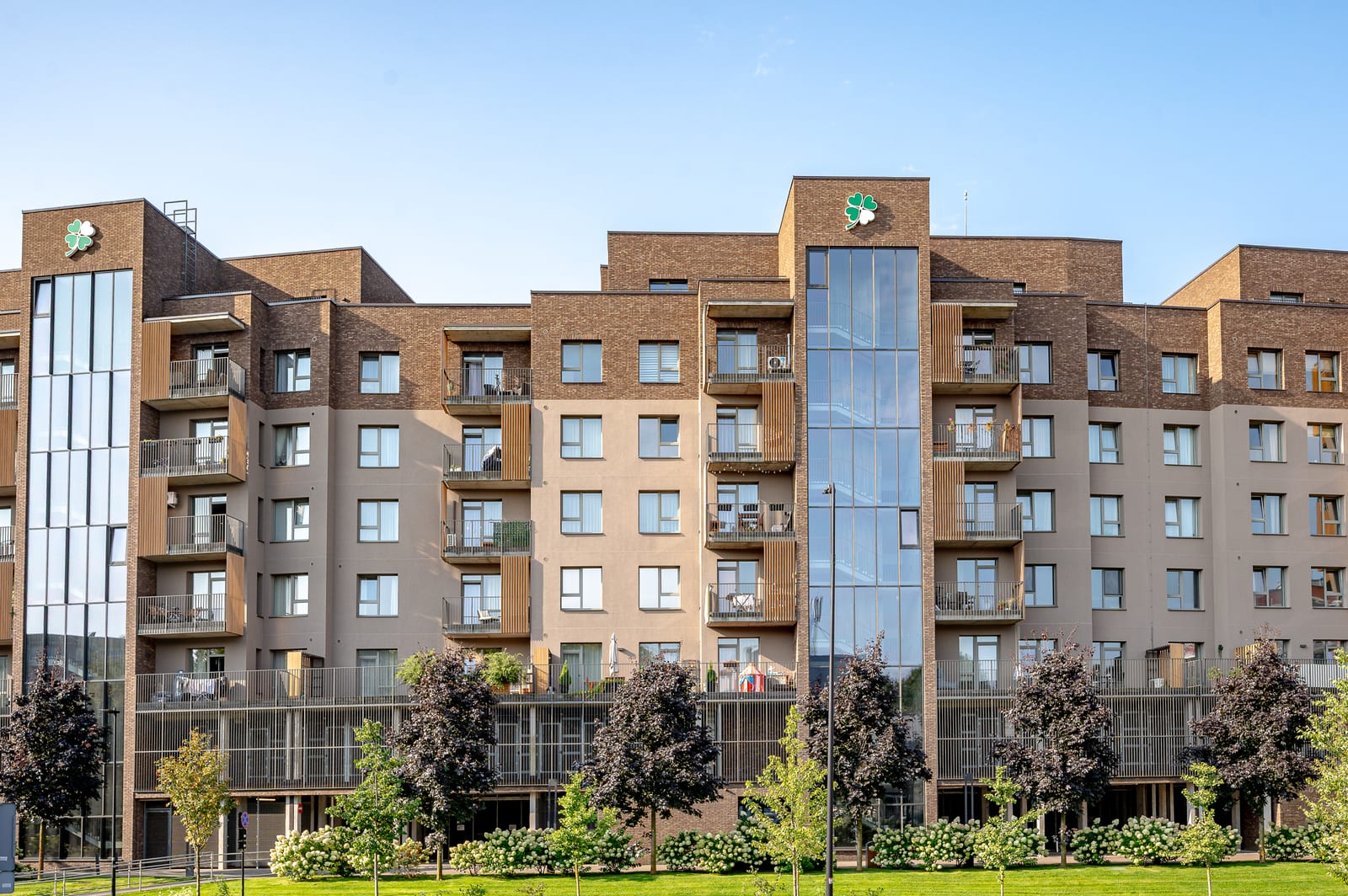 Lucky Homes by SAVO in Vilnius: de hele rij blokken in klinkerbaksteen met een glazen traptoren, gezien vanaf het gazon