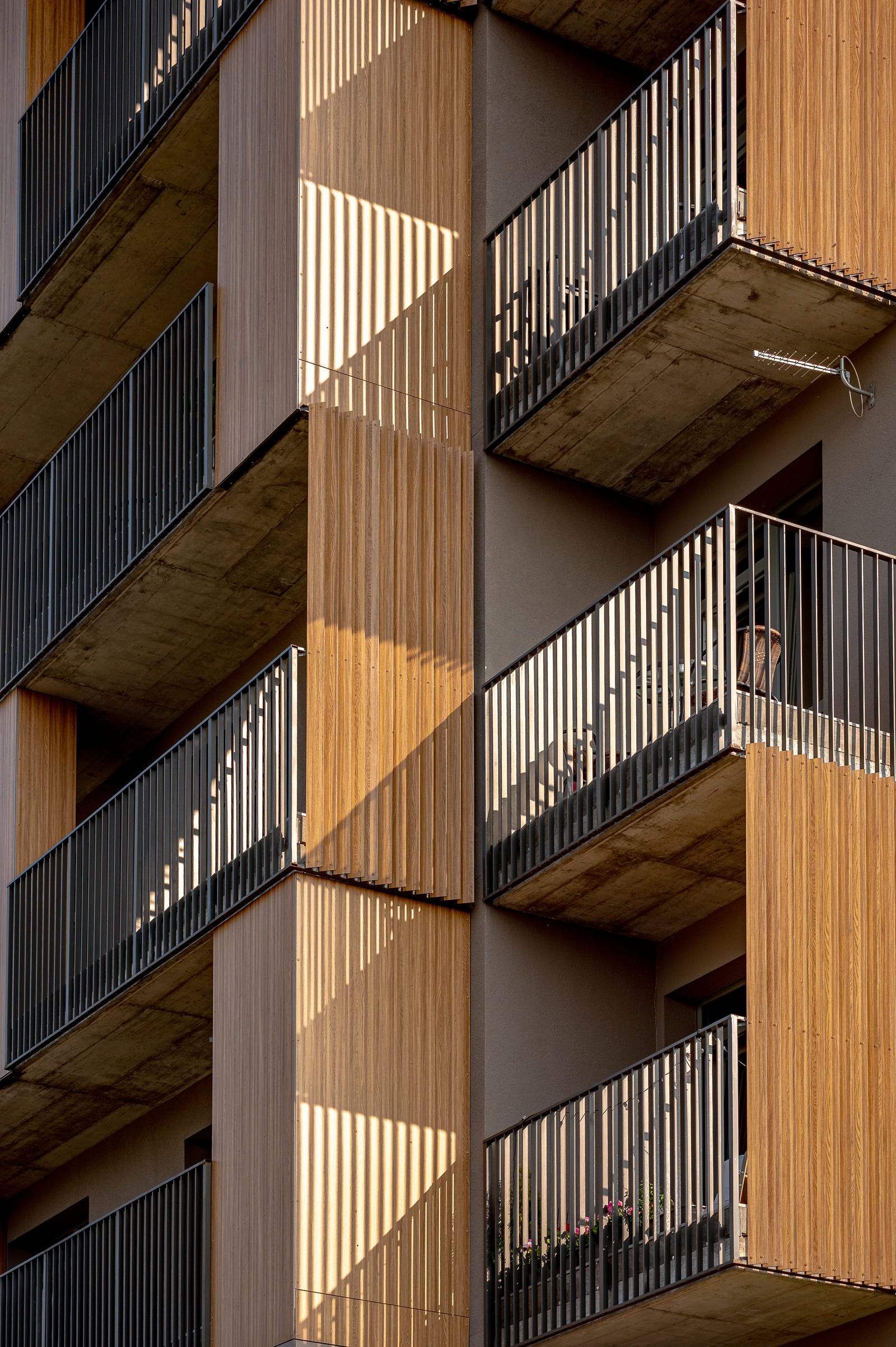 Detailopname van het SAVO-gebouw in Vilnius: gestapelde balkons met houtbekleding en zichtbeton in het late middaglicht